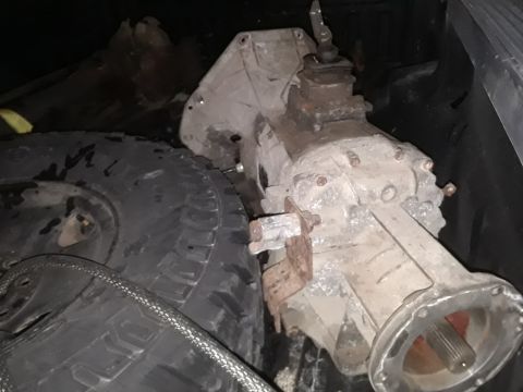 1994 Ford Bronco - A close-up view of a vehicle transmission and a tire, likely stored in a truck bed.