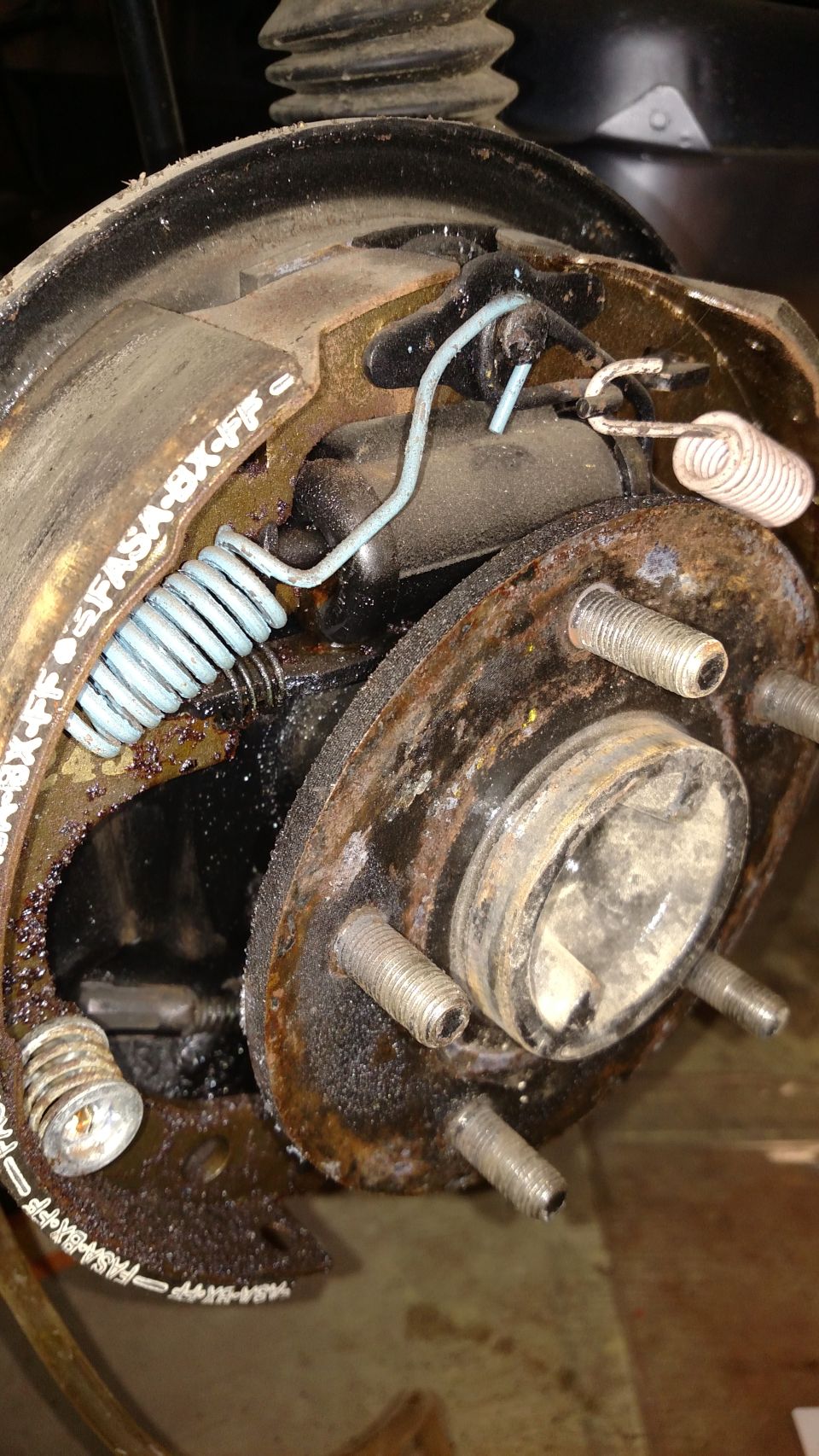 Close-up of a car's rear brake drum assembly with shoes and springs. Text 'FASA-BX-FF' is visible on the brake shoe
