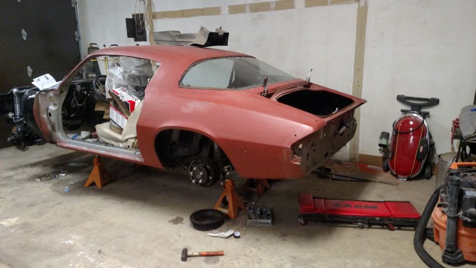Red 1977 Chevrolet Camaro undergoing restoration, missing doors and hood, on jack stands