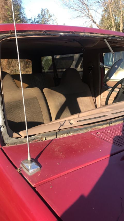1994 Ford Bronco - The interior of a red SUV is visible, with a missing windshield and worn seats.