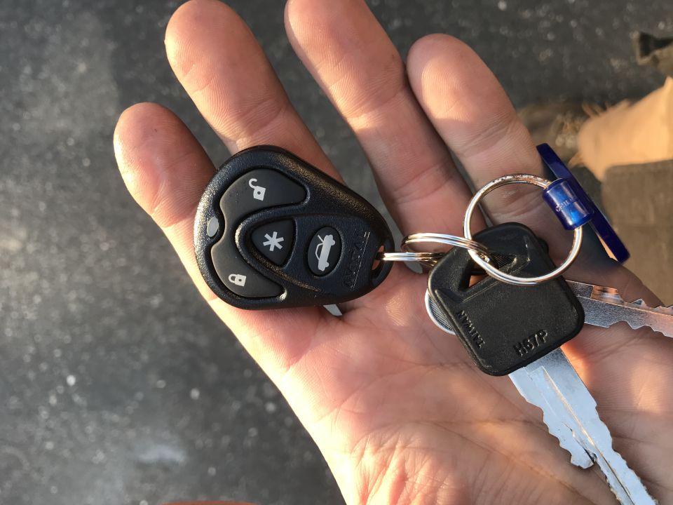Hand holding a key fob with lock, unlock, trunk, and panic buttons, plus two keys