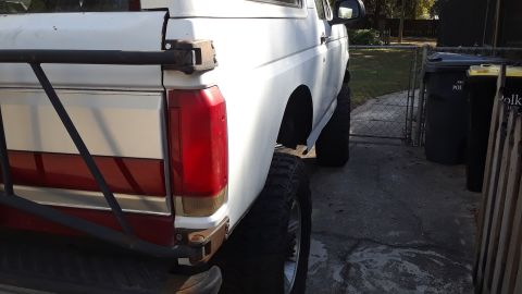 1994 Ford Bronco - This white Ford Bronco features a red stripe and aftermarket modifications, viewed from its rear quarter panel.