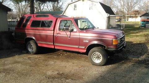 1991 Ford F-150 - A red 1991 Ford F-150 pickup truck with a red camper shell is parked in a dirt lot.