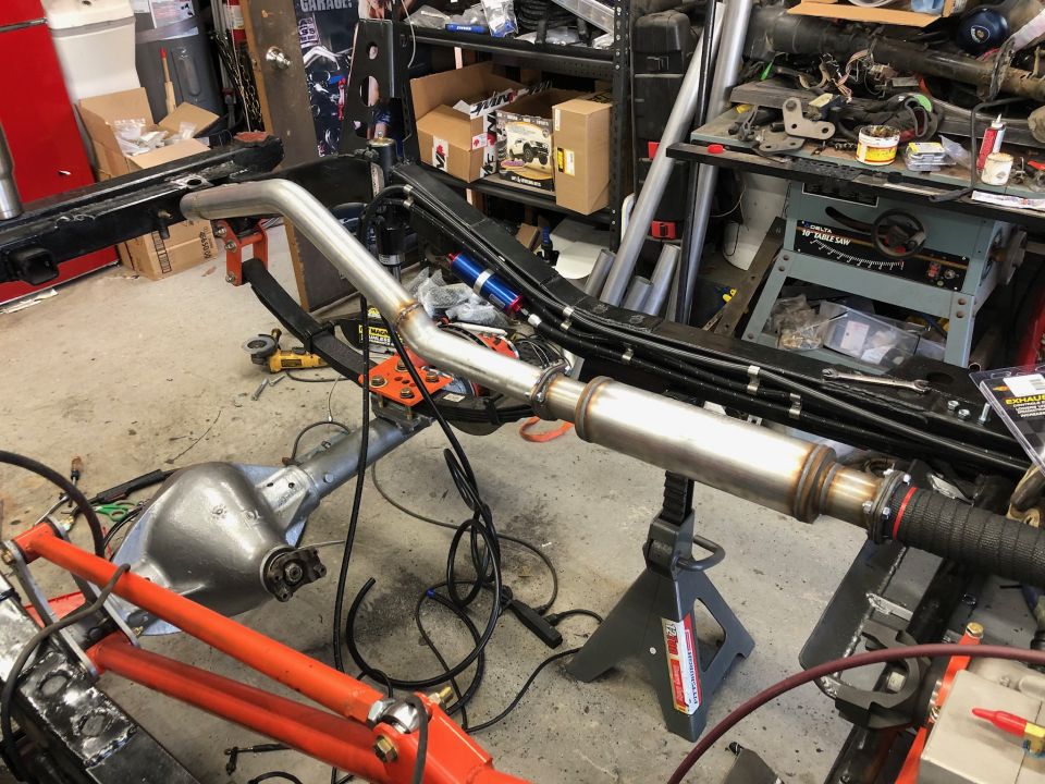 Exhaust pipe and muffler assembly supported by jack stands, with a rear axle and frame components visible