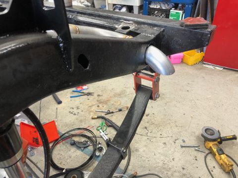 1992 Jeep Wrangler - Close-up view of an exhaust pipe tip being fitted to a vehicle's frame, with tools and parts scattered around the workshop floor.