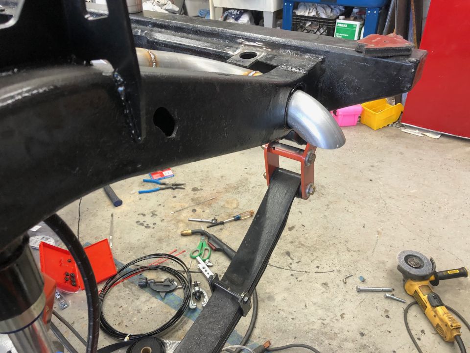 Exhaust pipe tip welded to vehicle frame with leaf spring visible