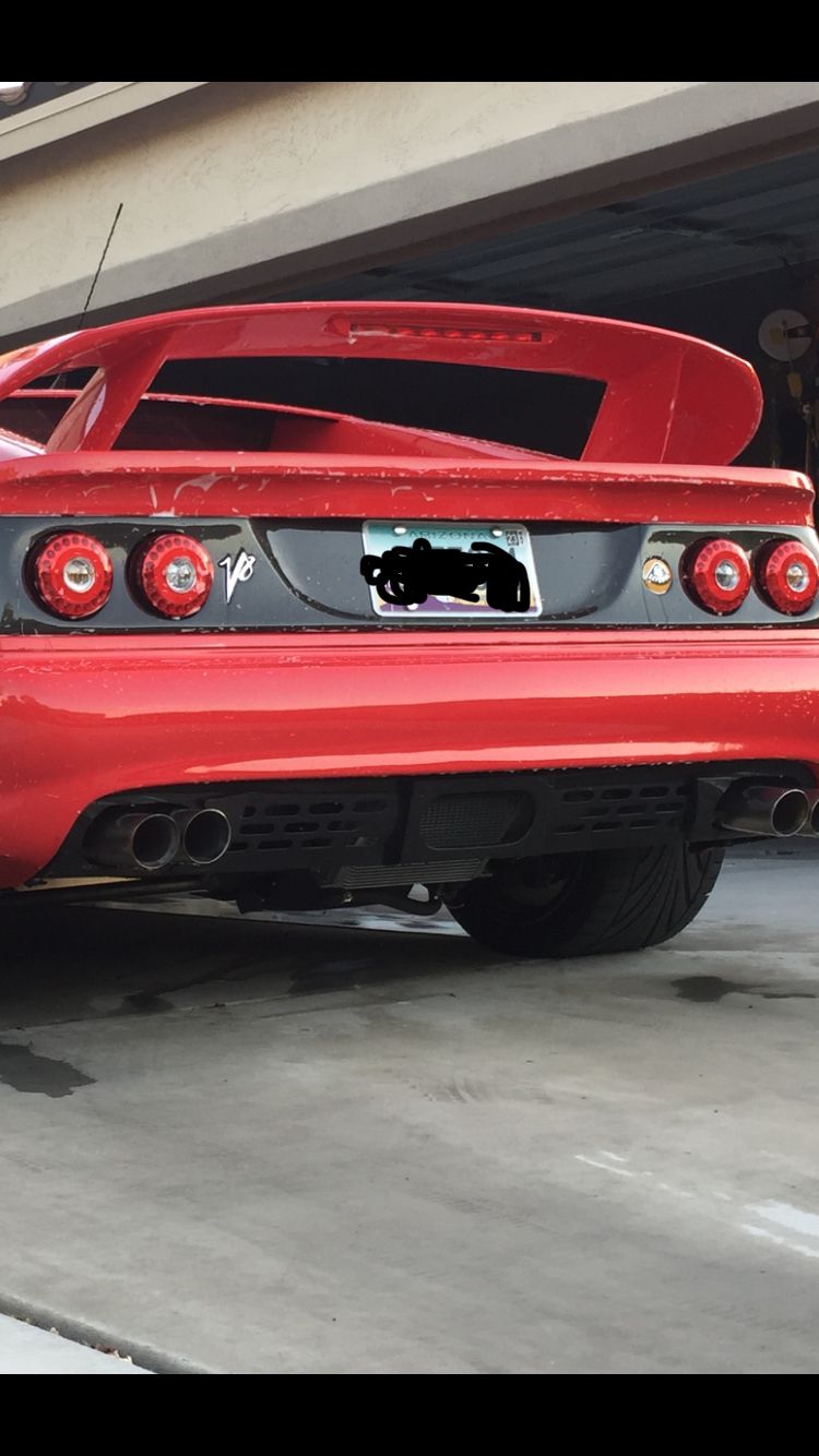Red sports car rear with spoiler, quad exhaust, and V8 badge. Likely a 1999 model