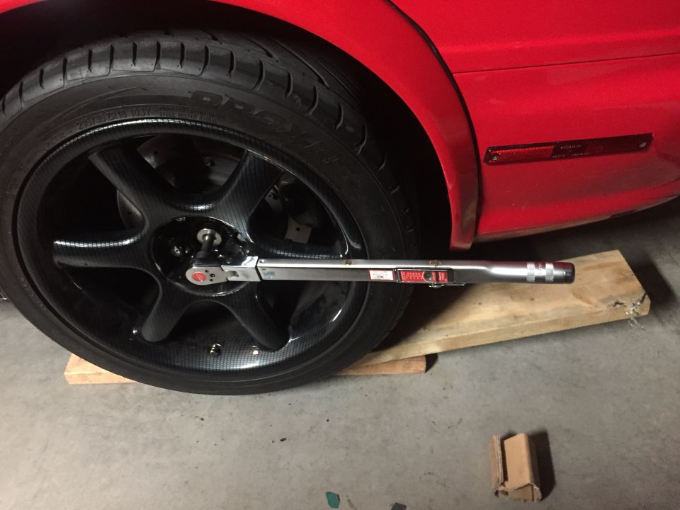 Using a torque wrench on a car's wheel, which is resting on wooden blocks