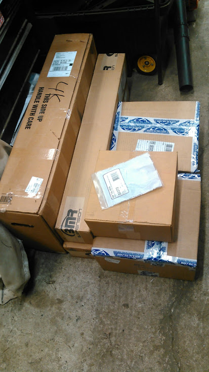 1978 Ford Bronco - Several cardboard boxes are stacked on a concrete floor. Some boxes have shipping labels and tape with blue lettering.