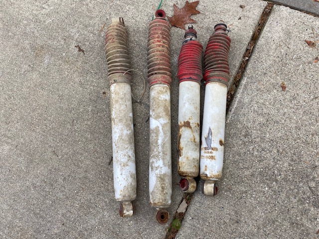 Four used white and red shock absorbers on concrete.