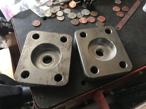 1989 Ford Bronco - Two metal flanges with four bolt holes each and a central recess sit on a workbench next to scattered coins.