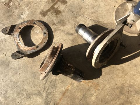 1989 Ford Bronco - Several rusty metal parts, possibly from a vehicle's suspension or drivetrain, are laid out on a concrete surface. One part appears to be a…