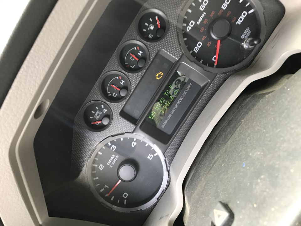 Close-up of a truck's dashboard with speedometer, tachometer, fuel gauge, and oil pressure gauge. The digital display shows '329 MILES TO E' and odometer reading '87282.2'