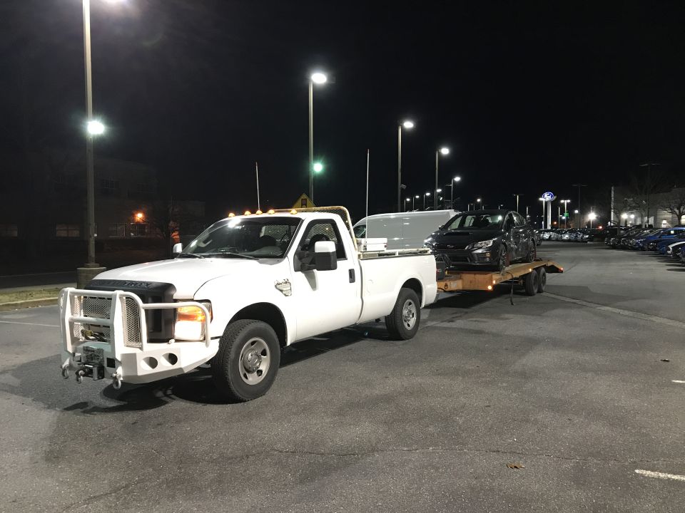 White Ford F-250 pickup truck towing a dark sedan on a trailer at night.