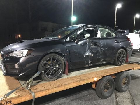 2008 Ford F-250 - A dark gray sedan with significant damage to the driver's side doors and body panels is loaded onto a flatbed tow truck at night. The vehic…