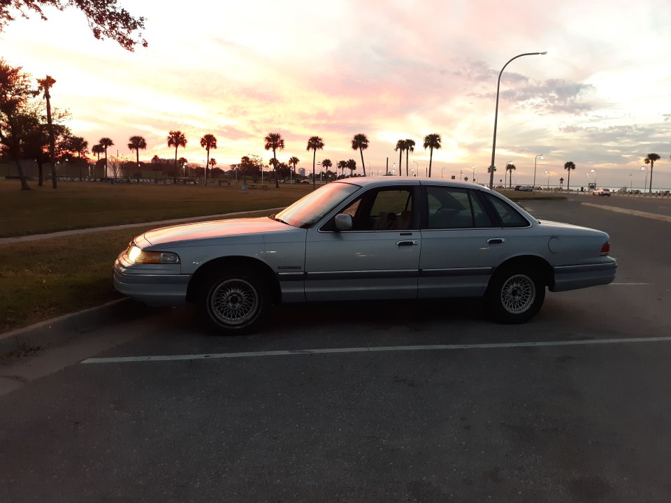 Silver 1994 Ford Crown Victoria sedan parked at sunset with palm trees.
