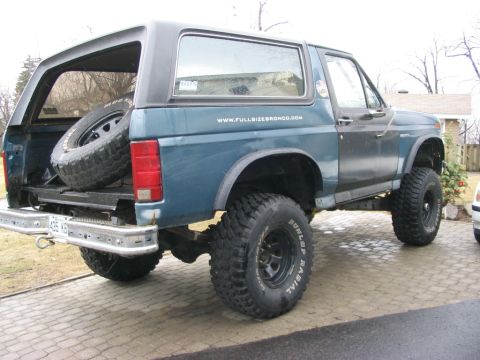 1986 Ford Bronco - Rear view of a 1986 Ford Bronco, showing the spare tire stored in the cargo area. The website www.fullsizebronco.com is visible on the side.