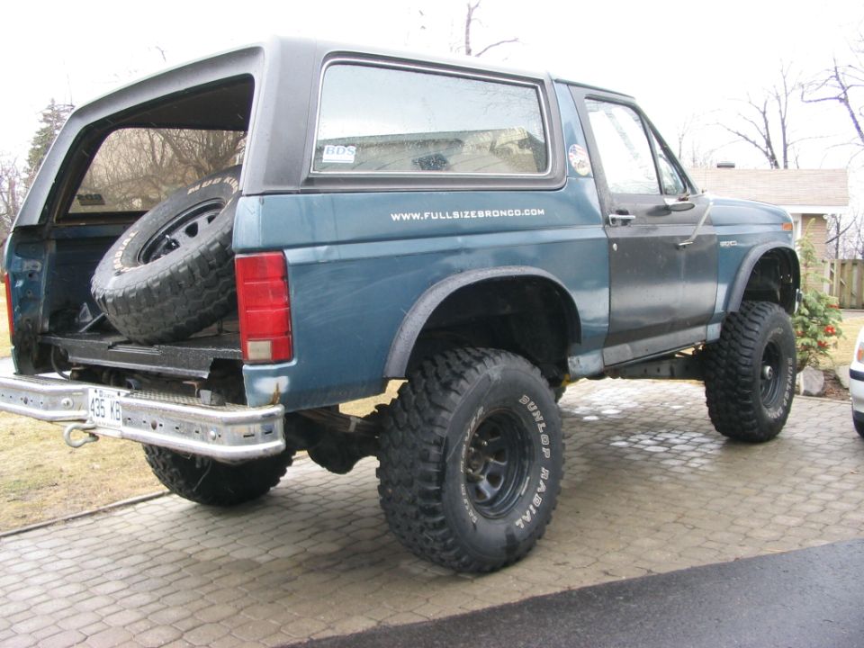 Lifted blue Ford Bronco with fender flares and tailgate down parked on a paver driveway