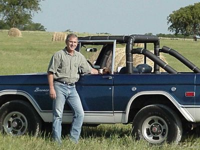 1993 Ford Bronco - A man poses with a blue Ford Bronco in a grassy field with hay bales in the background.