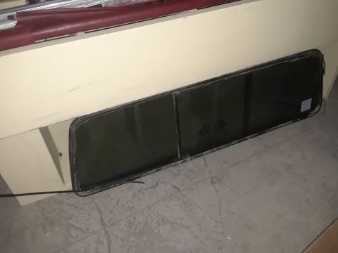 1994 Ford Bronco - A dark tinted, rectangular window with a black rubber seal is shown resting on a concrete floor. The window appears to be a replacement par…