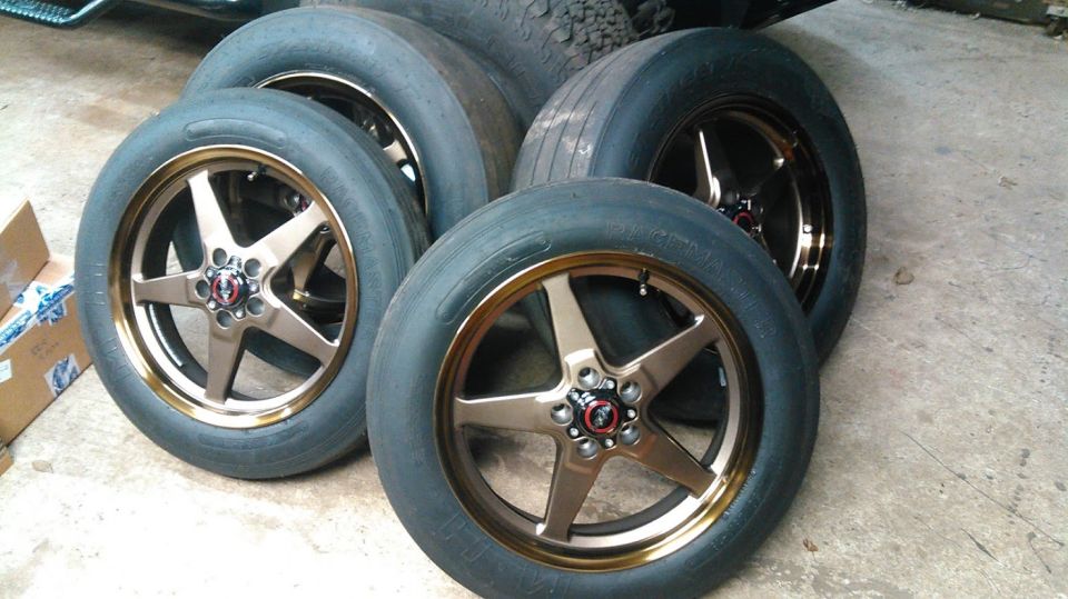Four bronze five-spoke racing wheels with black tires on a concrete floor.