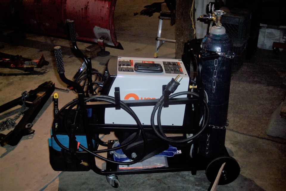 Welding machine cart with gas cylinder and accessories in a garage.