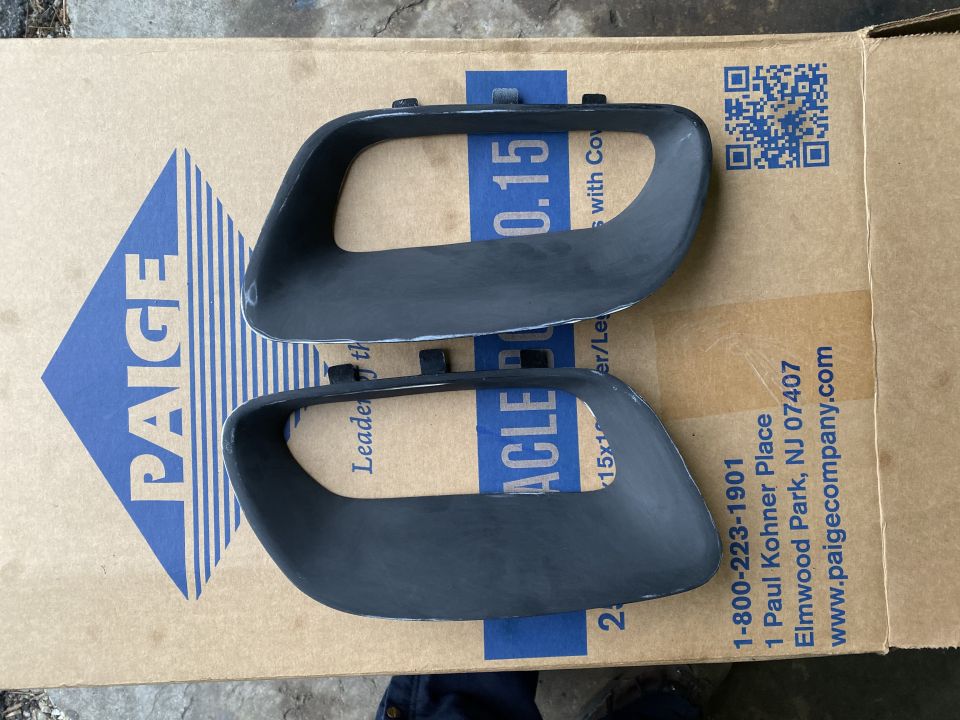 Two dark gray automotive trim pieces on a cardboard box.