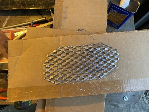 Perforated metal mesh on cardboard with tools and mineral spirits in background