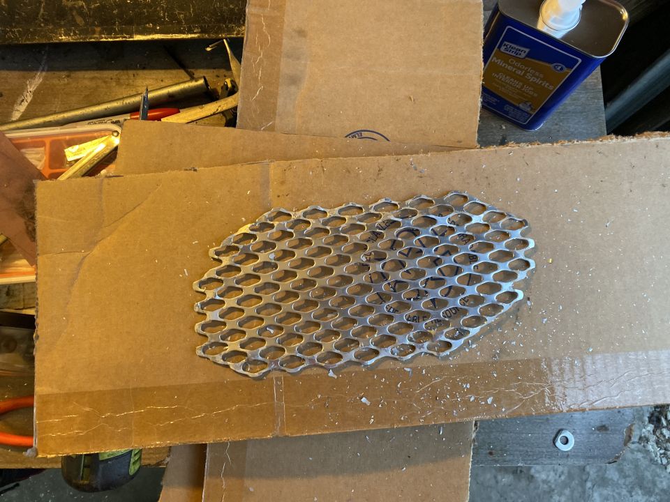 Perforated metal mesh on cardboard with tools and mineral spirits in background