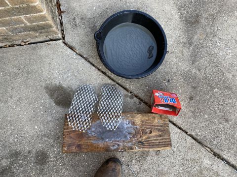 Bucket of water, wooden plank with mesh grates, and Brillo soap pads on concrete.