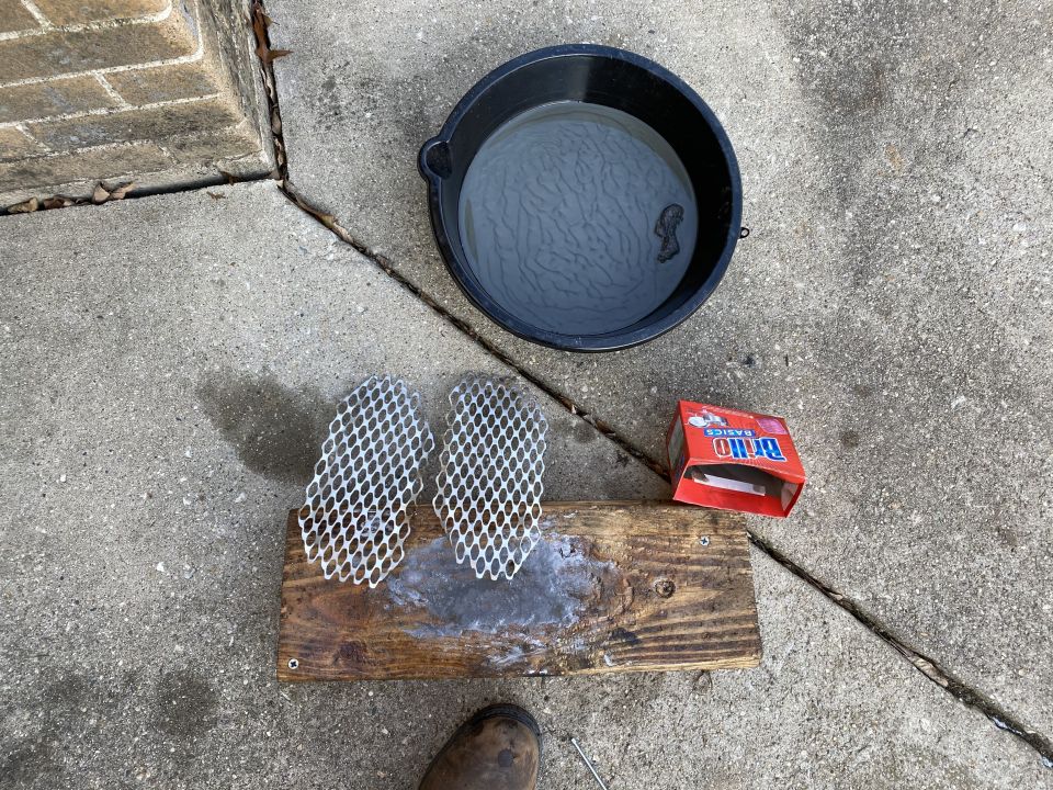 Bucket of water, wooden plank with mesh grates, and Brillo soap pads on concrete.
