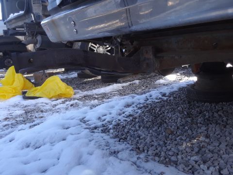 1994 Ford Bronco - The underside of a vehicle, likely a 1994 Ford Bronco, is shown with a rusty frame and bumper assembly. Yellow plastic bags are visible on…