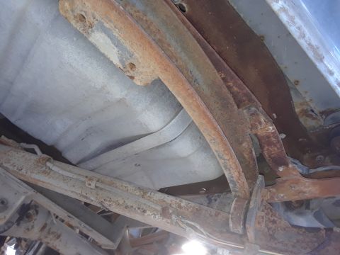 1994 Ford Bronco - The underside of a vehicle shows a heavily rusted fuel tank and suspension components, including leaf springs and frame brackets. Metal sur…