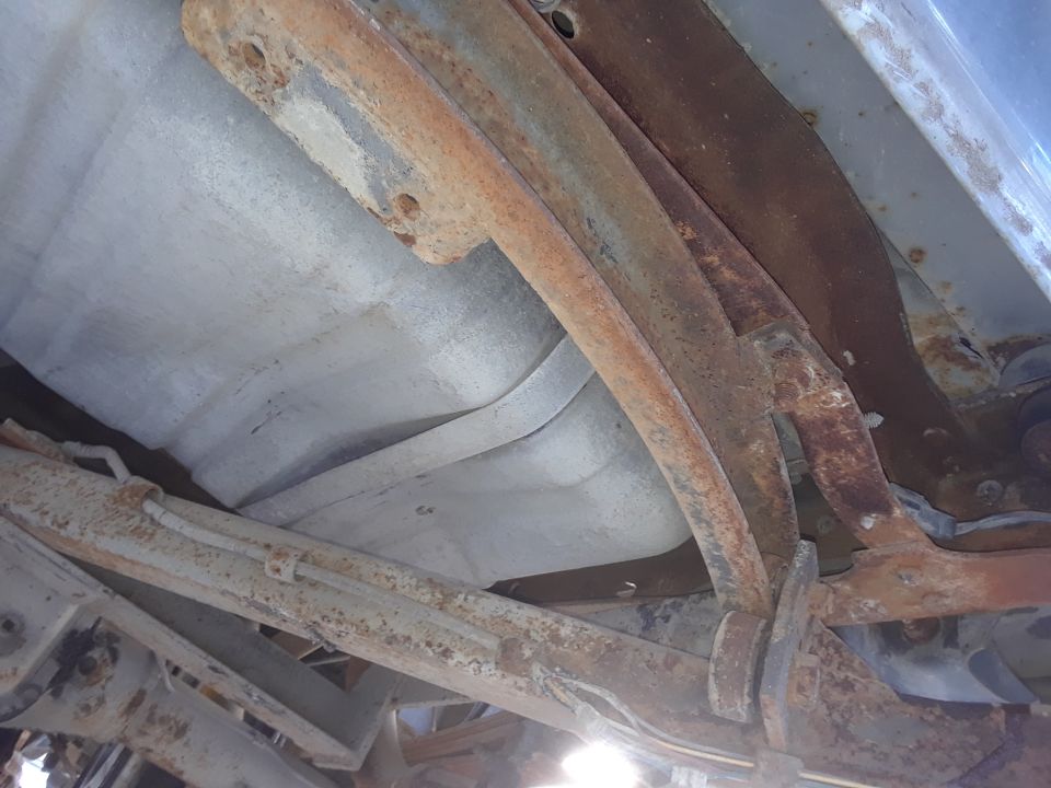 Underside of a vehicle with rusted fuel tank and suspension components.
