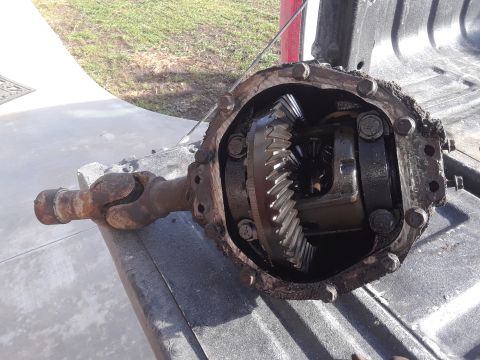 1994 Ford Bronco - A differential assembly with a driveshaft attached is shown, resting on a textured surface, likely a truck bed. The differential housing is…