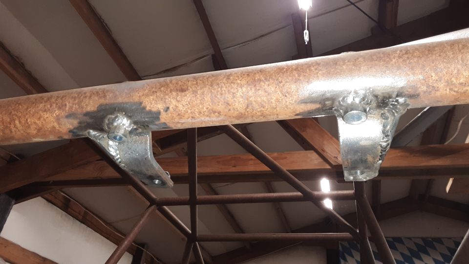 Welded metal brackets attached to a rusty pipe suspended from a ceiling.