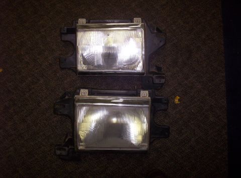 1988 Ford Bronco - A pair of vehicle headlight assemblies are displayed on a dark, textured surface.