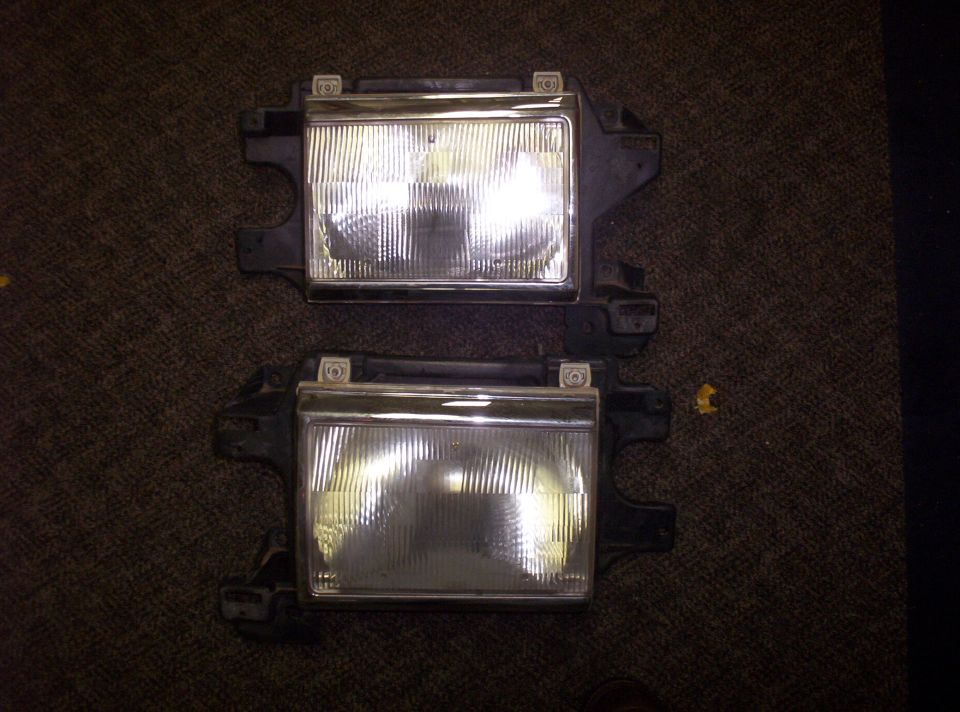 Two vehicle headlight assemblies are shown against a dark carpeted background