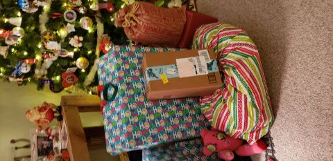 1965 Ford Mustang - A Christmas tree decorated with ornaments and lights stands next to several wrapped gifts. One gift is a cardboard box with shipping labels…