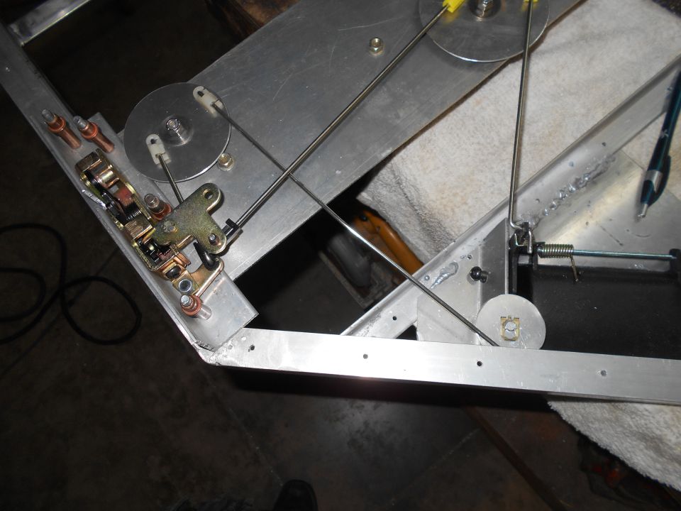 Close-up of mechanical assembly with cables, pulleys, and latch on aluminum frame.