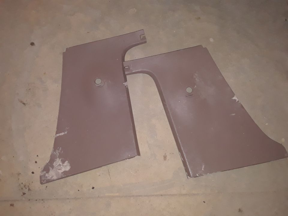 Two brown plastic interior trim panels with circular mounting holes, lying on a concrete floor