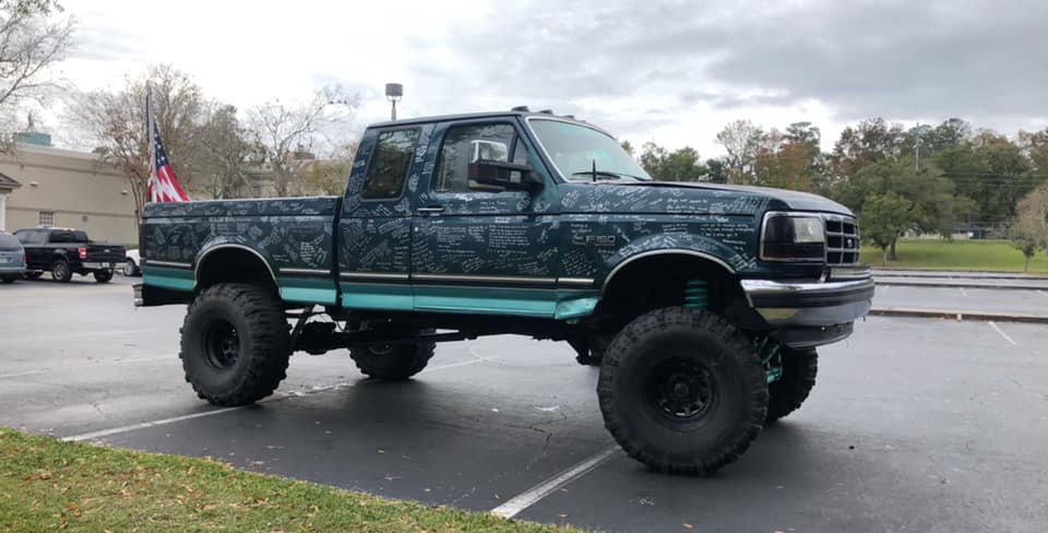 Lifted Ford pickup with custom graphics and large tires. An American flag is in the truck bed