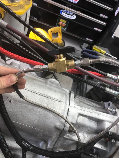 1992 Jeep Wrangler - A hand holds a braided hose connected to a brass valve assembly on an engine.