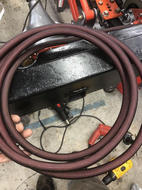 1992 Jeep Wrangler - A close-up shot shows a coiled braided hose, likely for a vehicle's hydraulic system, resting on a black metal component. Various tools, in…