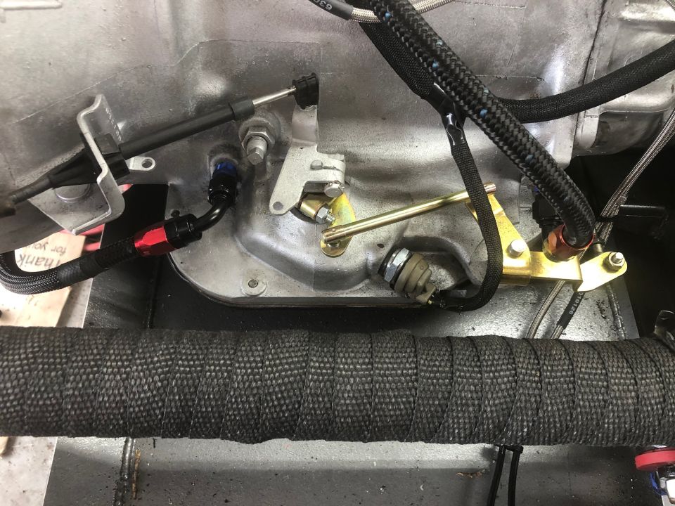Close-up of engine components with throttle cable, fuel line, and brass linkage.