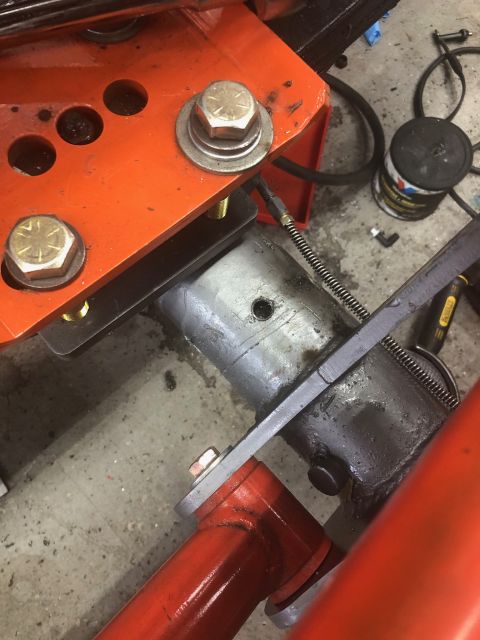1992 Jeep Wrangler - A close-up view shows a hydraulic cylinder assembly attached to an orange metal bracket with large bolts. A black spring is visible, connec…