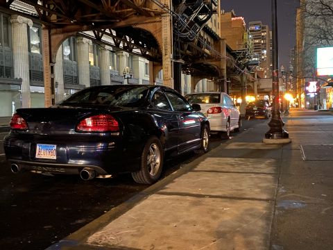 Dark blue Pontiac Grand Prix parked on a city street at night, rear view.