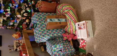 1965 Ford Mustang - A collection of Christmas presents are piled around the base of a decorated Christmas tree. The presents are wrapped in festive paper, incl…