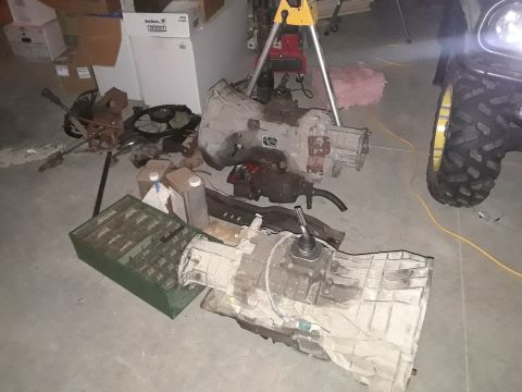 1994 Ford Bronco - Two large transmission assemblies are laid out on a concrete floor, along with various automotive parts including a fan and some fluid cont…