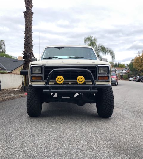 1981 Ford Bronco - Front view of a lifted, cream-colored Ford Bronco with a black brush guard featuring two yellow auxiliary lights with smiley faces. The tru…